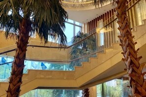 A multi-level interior with glass railings, palm trees, and a staircase. - Yushan Hotel (Changshu)