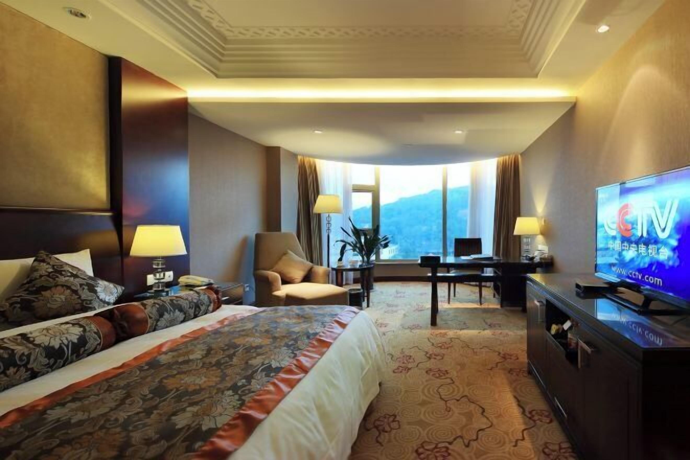 Een hotelkamer met een groot bed, een bureau, een stoel, een televisie en uitzicht op de bergen.