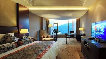 Een hotelkamer met een groot bed, een bureau, een stoel, een televisie en uitzicht op de bergen.