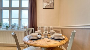 A dining area with a round wooden table set for four, surrounded by white chairs. - Harrow Croft, 2 Bedroom Flat St Johns, Worcester (Worcestershire)