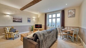 A cozy living room with a sofa, armchair, and dining table. A TV is on, displaying 'NETFLIX'. - Harrow Croft, 2 Bedroom Flat St Johns, Worcester (Worcestershire)