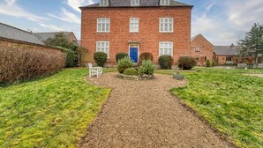A brick house with a blue door, surrounded by a gravel path and green grass. - Harrow Croft, 2 Bedroom Flat St Johns, Worcester (Worcestershire)