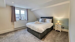 A bedroom with a bed, a nightstand, a window with curtains, and a radiator. - Harrow Croft, 2 Bedroom Flat St Johns, Worcester (Worcestershire)