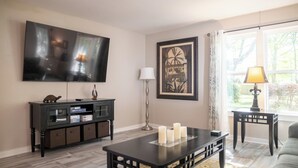 A living room with a flat-screen TV, a framed picture, a coffee table with candles, a side table with a lamp, and a sofa. - 3BR/2.5BA close to Beach, Casinos & Downtown Ocean Springs! Shorebound (Ocean Springs)
