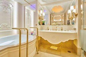 Un baño lujoso con una bañera grande, un tocador con espejo y detalles dorados.