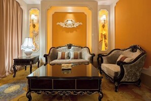 Une pièce comprenant une table avec un plateau en verre, deux fauteuils rembourrés, une petite table d’appoint avec une lampe et un élément décoratif mural.