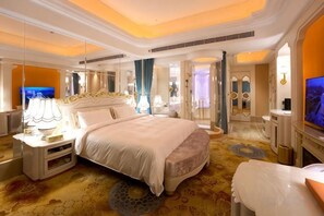 Una habitación de hotel amplia con una cama grande, televisión y baño con espejo y lavamanos.