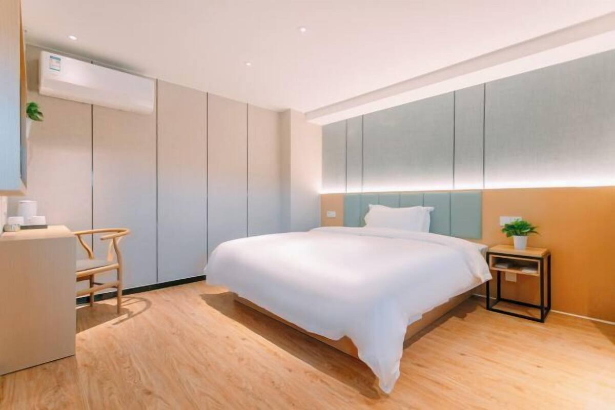 A modern hotel room with a large bed, a desk, and a small side table with a plant.