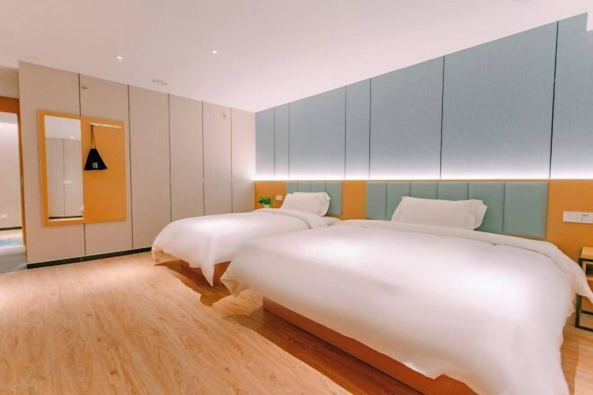 A modern hotel room with a large bed, a bedside table, a mirror, and a wall-mounted light fixture.