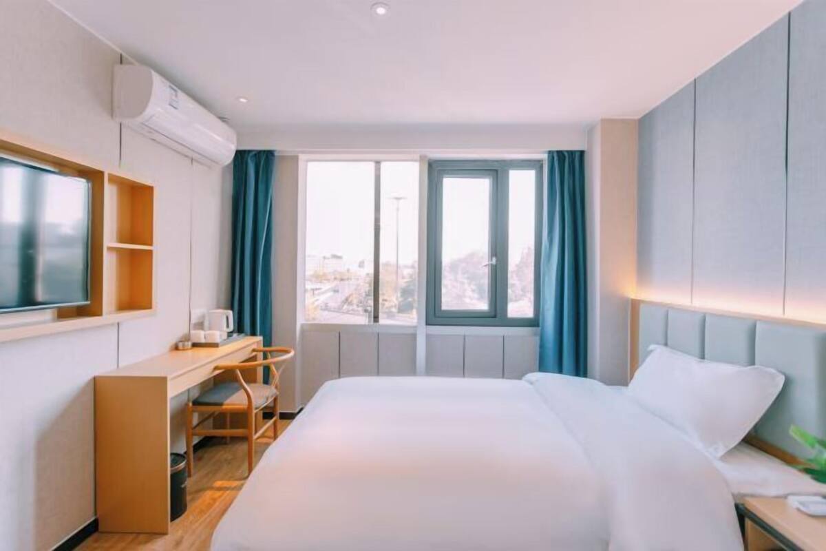A hotel room with a bed, a desk, a chair, a TV, and a window with curtains.