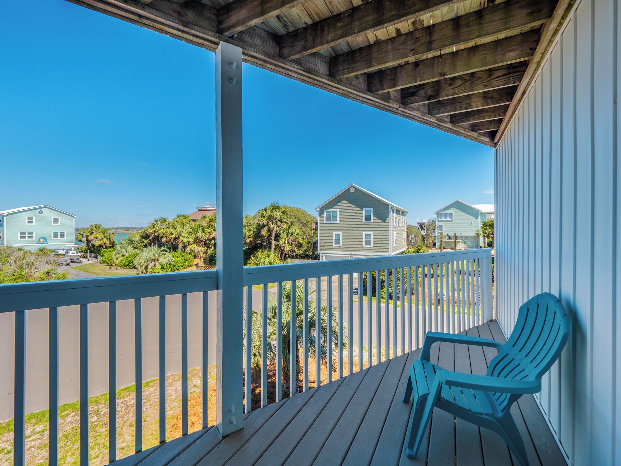 A wooden deck with a blue chair, overlooking a residential area with houses and palm trees.