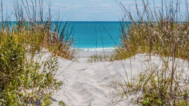 A sandy beach with clear blue water and sparse vegetation. - The Channel Marker by Topsail Realty (Holly Ridge)