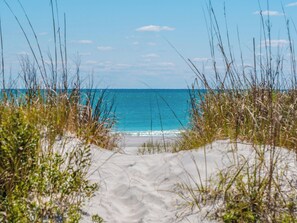 A sandy beach with clear blue water and sparse vegetation. - The Channel Marker by Topsail Realty (Holly Ridge)
