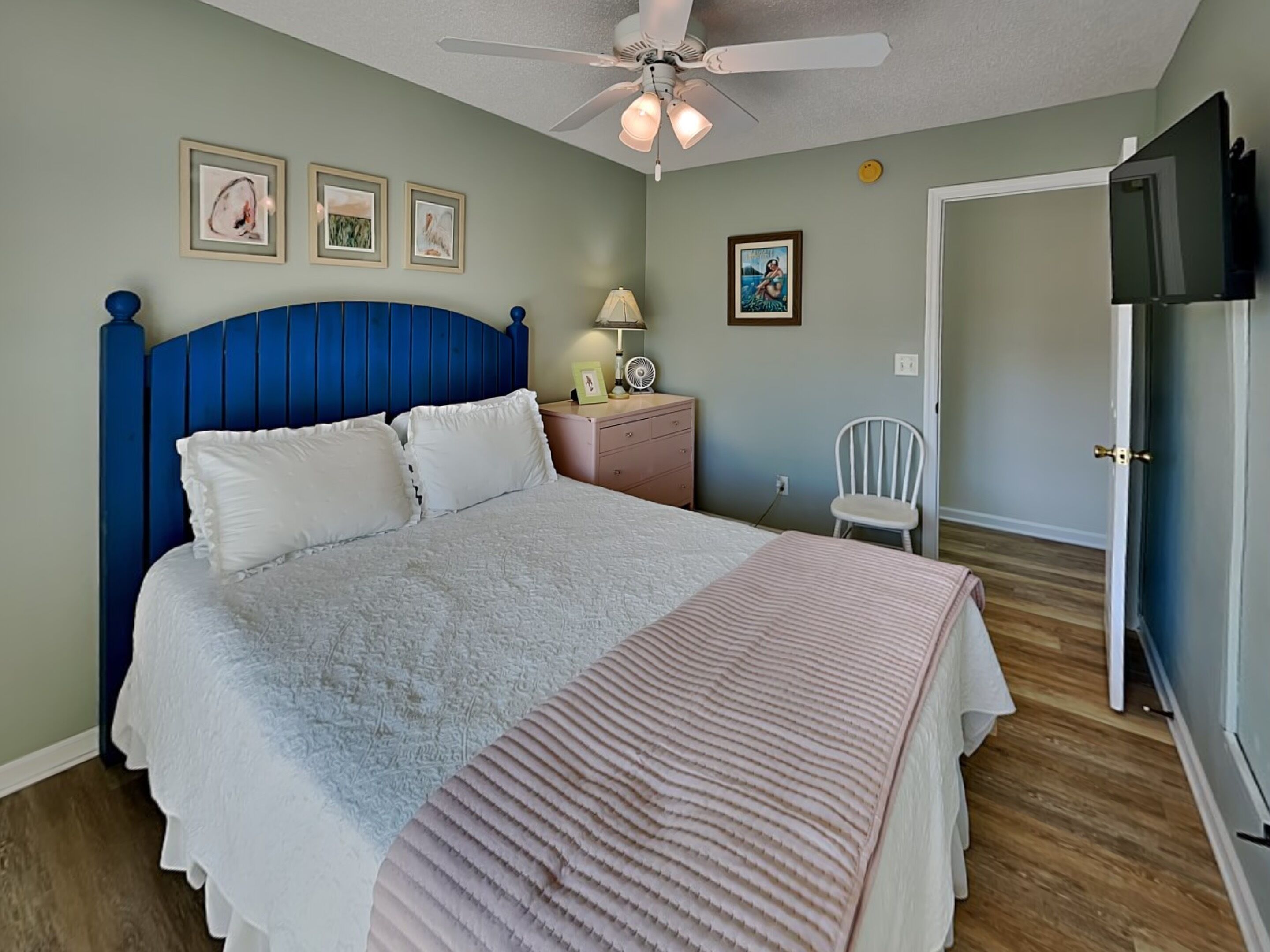 A bedroom with a bed, a nightstand, a chair, a ceiling fan, and a TV.