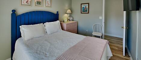 A bedroom with a bed, a nightstand, a chair, a ceiling fan, and a TV.