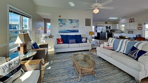A spacious living room with a large window, a ceiling fan, and a nautical-themed painting. - The Channel Marker by Topsail Realty (Holly Ridge)