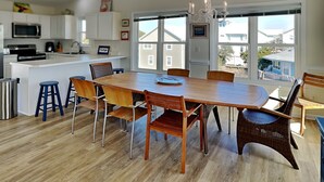 A modern kitchen with white cabinets, a central island, and a dining area with a wooden table and wicker chairs. - The Channel Marker by Topsail Realty (Holly Ridge)