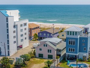 A coastal residential area with a beach view, including a house with a pool and a building with a balcony overlooking the ocean. - Beach Breeze by Carolina Retreats (Carolina Beach)