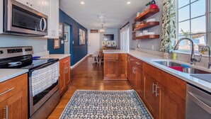 A modern kitchen with wooden cabinets, stainless steel appliances, and a large window with a view. - Beach Breeze by Carolina Retreats (Carolina Beach)