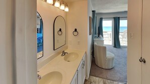 A modern bathroom with dual sinks, a large mirror, and a vanity. A balcony with a view of the sea is visible through the door. - Hailey's Hideaway by Topsail Realty (Holly Ridge)