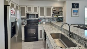 A modern kitchen with white cabinets, stainless steel appliances, a granite countertop, and a built-in sink. - Hailey's Hideaway by Topsail Realty (Holly Ridge)