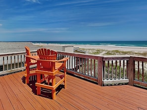 A wooden deck with a wooden chair, overlooking a beach with sand and water. - Paradise Palms by Topsail Realty (Holly Ridge)