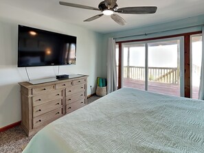 A bedroom with a large bed, a wooden dresser, a flat-screen TV mounted on the wall, and a ceiling fan. - Paradise Palms by Topsail Realty (Holly Ridge)