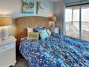 A bedroom with a bed, two nightstands, a woven headboard, and a view of the balcony. - Paradise Palms by Topsail Realty (Holly Ridge)