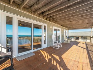 A covered deck with wooden flooring and glass doors leading to a beach view. - Paradise Palms by Topsail Realty (Holly Ridge)