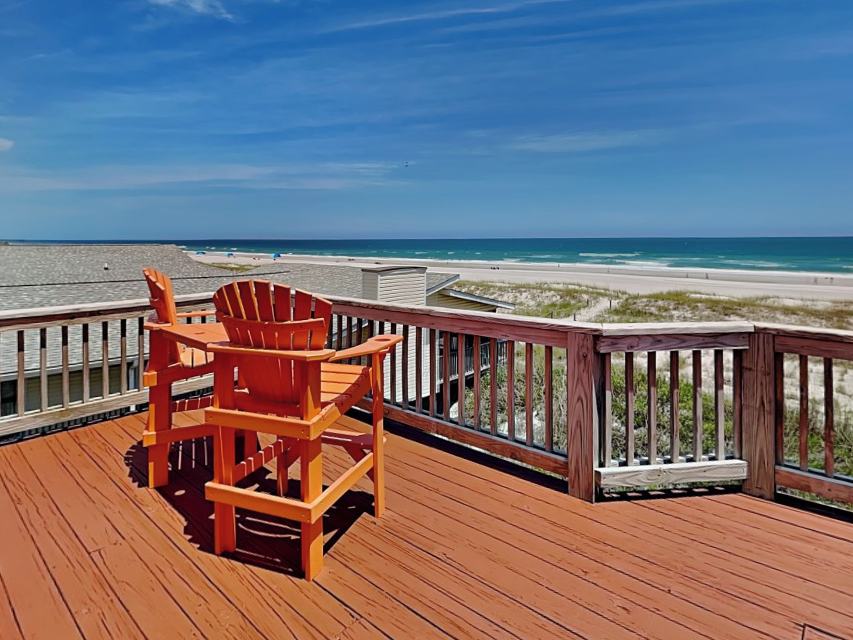 A wooden deck with a wooden chair, overlooking a beach with sand and water.