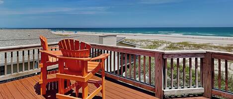 A wooden deck with a wooden chair, overlooking a beach with sand and water.