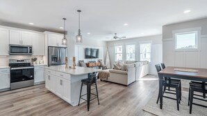 A modern kitchen with white cabinetry, stainless steel appliances, and pendant lighting. - Jersey Blues by Carolina Retreats (Carolina Beach)