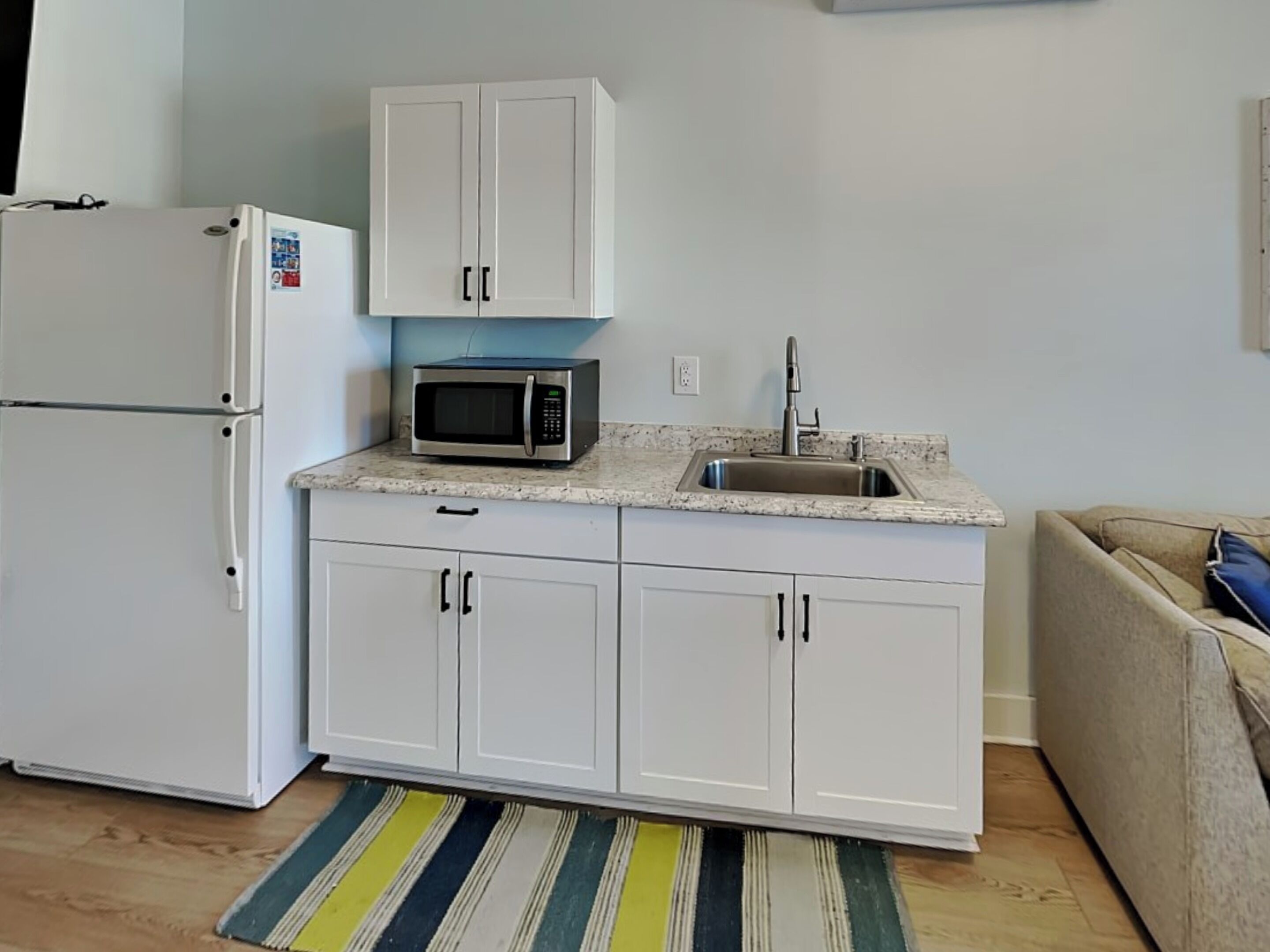 A compact kitchen with white cabinets, a stainless steel sink, a microwave, and a refrigerator.