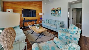 Una sala de estar con pared de madera, un televisor de pantalla plana, un sofá, una mesa de centro y un tapete estampado.