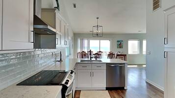 A modern kitchen with white cabinetry, a black stove, and a dining area with wooden chairs and a view of the ocean.