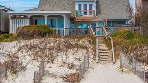 Et hus ved stranden med en overdækket veranda, en balkon på anden sal og en sandstrand i forgrunden.