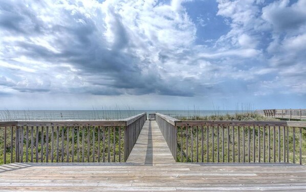 A wooden boardwalk leading to the beach with a cloudy sky above.