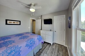 Ein Schlafzimmer mit Bett, Deckenventilator, Fernseher, Kleiderschrank und einer Tür.