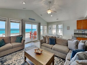 A spacious living room with a view of the ocean, two sofas, a coffee table, and a ceiling fan.