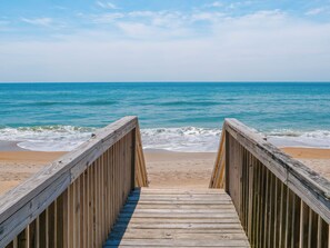 A wooden boardwalk leading to a beach with clear blue water and a sandy shore. - Some Beach by Topsail Realty (Holly Ridge)
