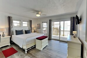 Un dormitorio con cama, mesitas de noche, alfombra roja, ventilador de techo y vistas a un balcón.
