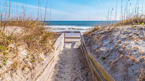 Un sentier en bois mène à une plage, et une rambarde en bois est installée sur un de ses côtés.