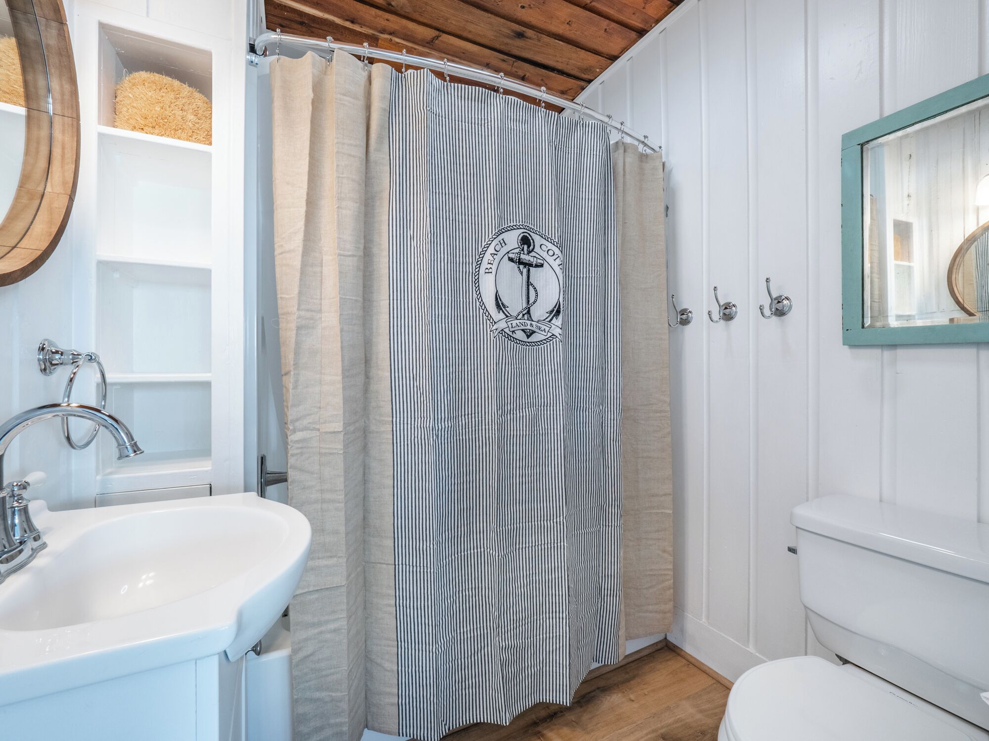 Un baño con lavamanos blanco, bañera, cortina de ducha con diseño náutico y retrete.