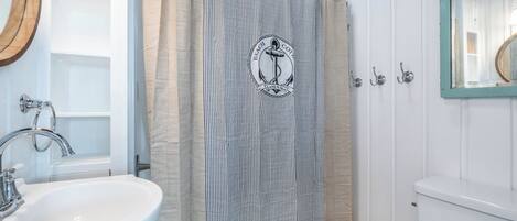 Un baño con lavamanos blanco, bañera, cortina de ducha con diseño náutico y retrete.