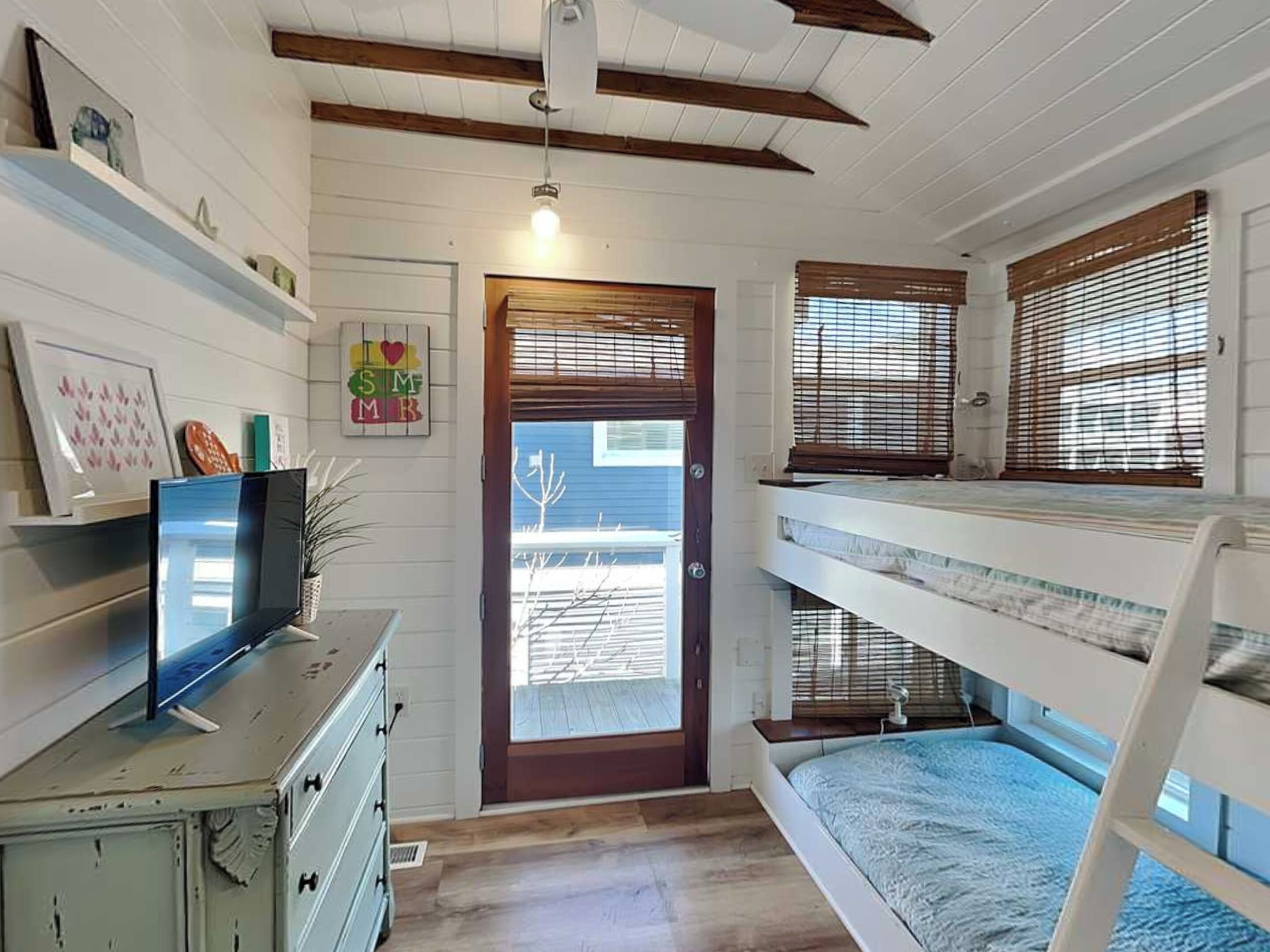 A room with bunk beds, a television on a dresser, a door with a window, and a wall with a 'I ❤️ SM' sign.