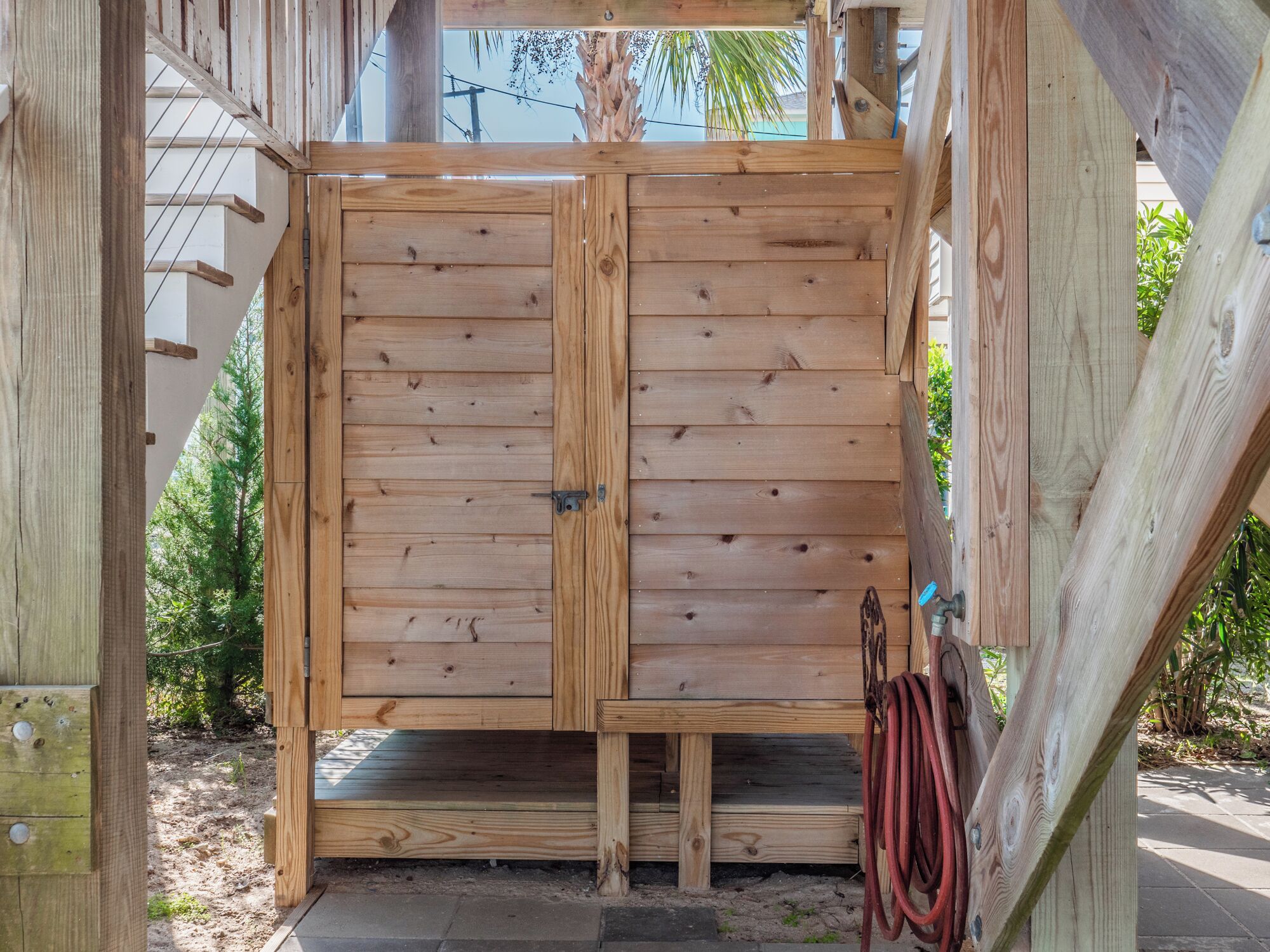 Una estructura de madera con una puerta corredera, una mesita y una manguera.