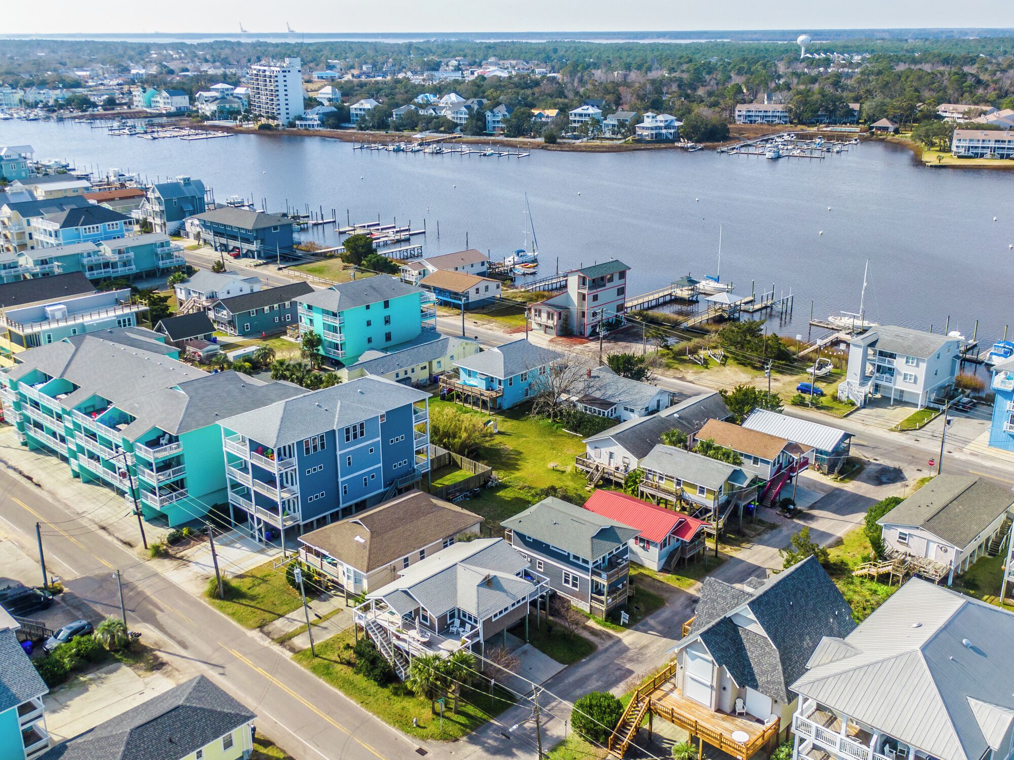 An aerial view of a coastal residential area with houses, a marina, and a lighthouse.