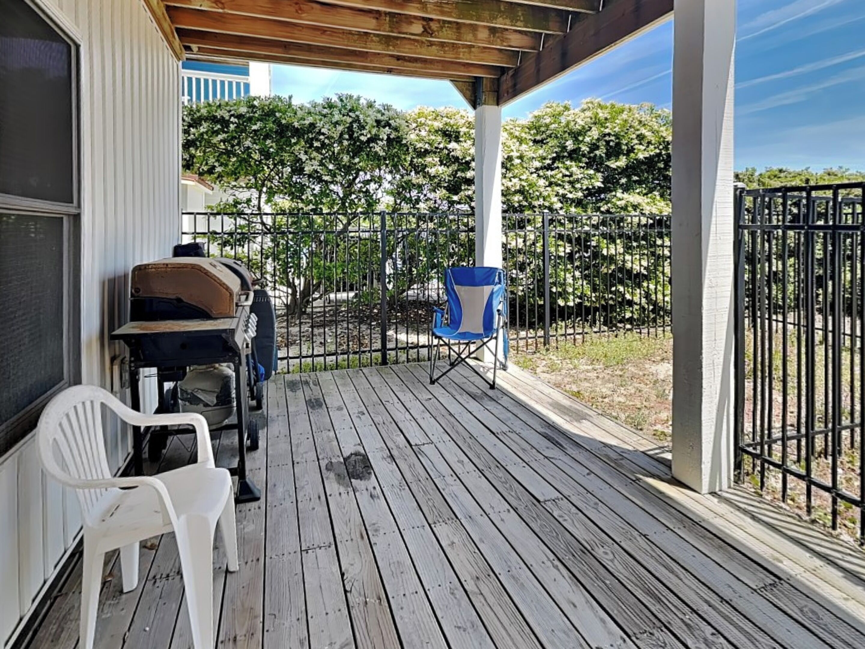 A wooden deck with a grill, a folding chair, and a white plastic chair.