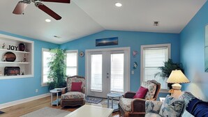 A living room with a ceiling fan, a white coffee table, two wicker chairs, a blue sofa, and a bookshelf with decorative items. - No Worries in Paradise (Carolina Beach)