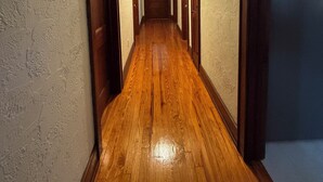 Un pasillo largo y estrecho con pisos de madera y puertas a ambos lados, que conduce a una habitación con ventana.